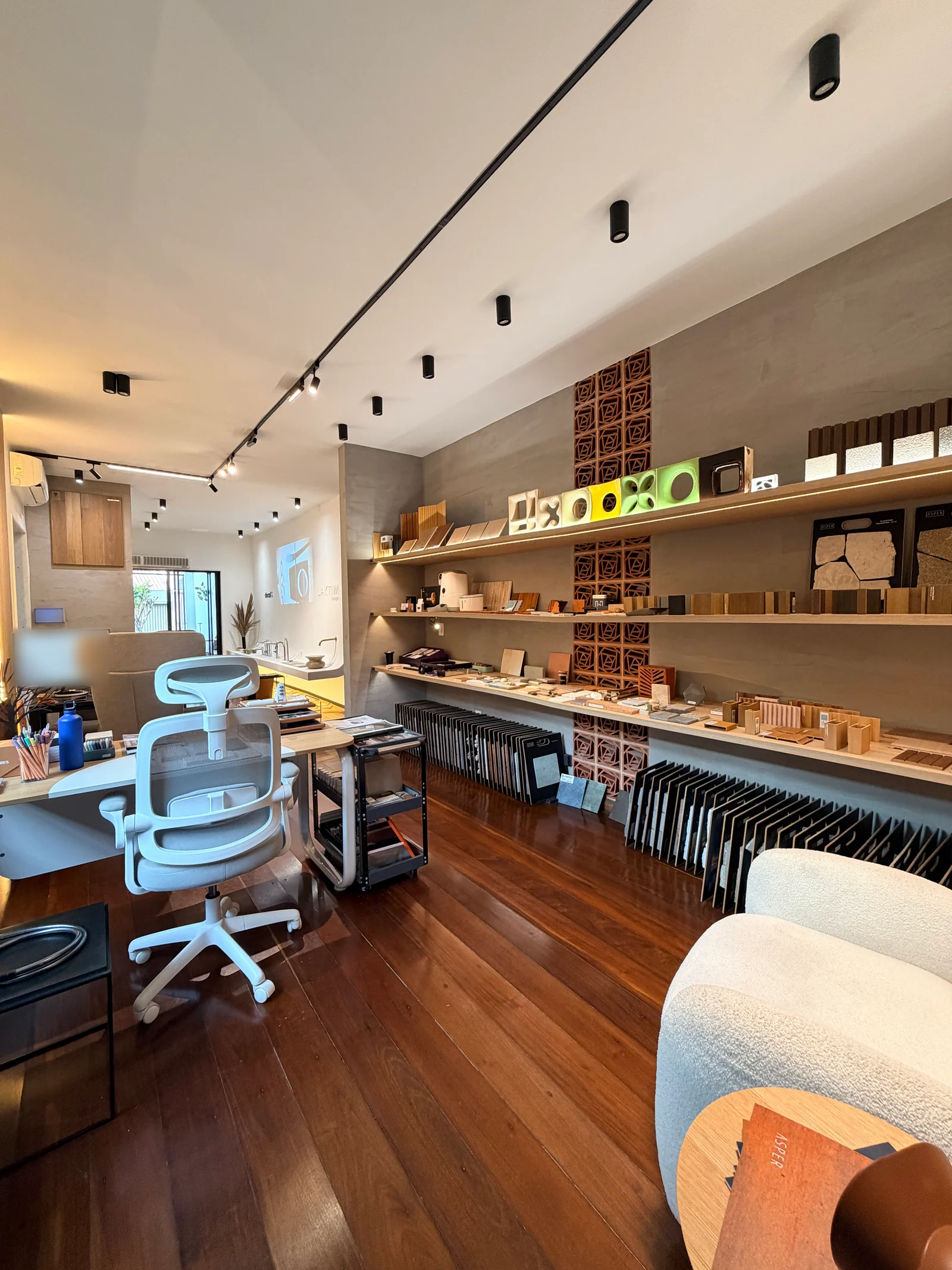 Showroom com prateleiras de amostras, cobogós, trilho de luz e piso de madeira
