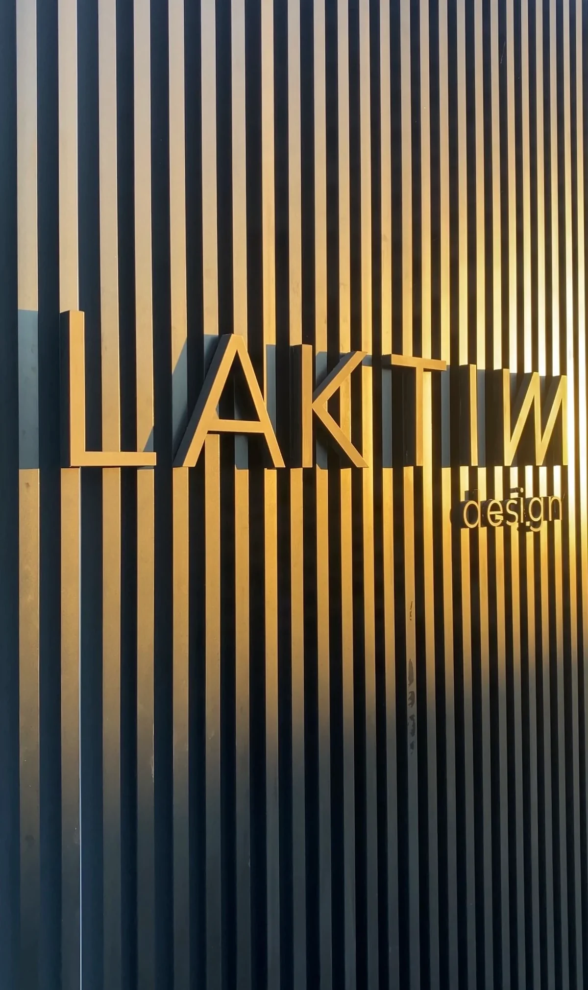 Fachada da Laktim Design: letreiro sobre ripas pretas ao pôr do sol